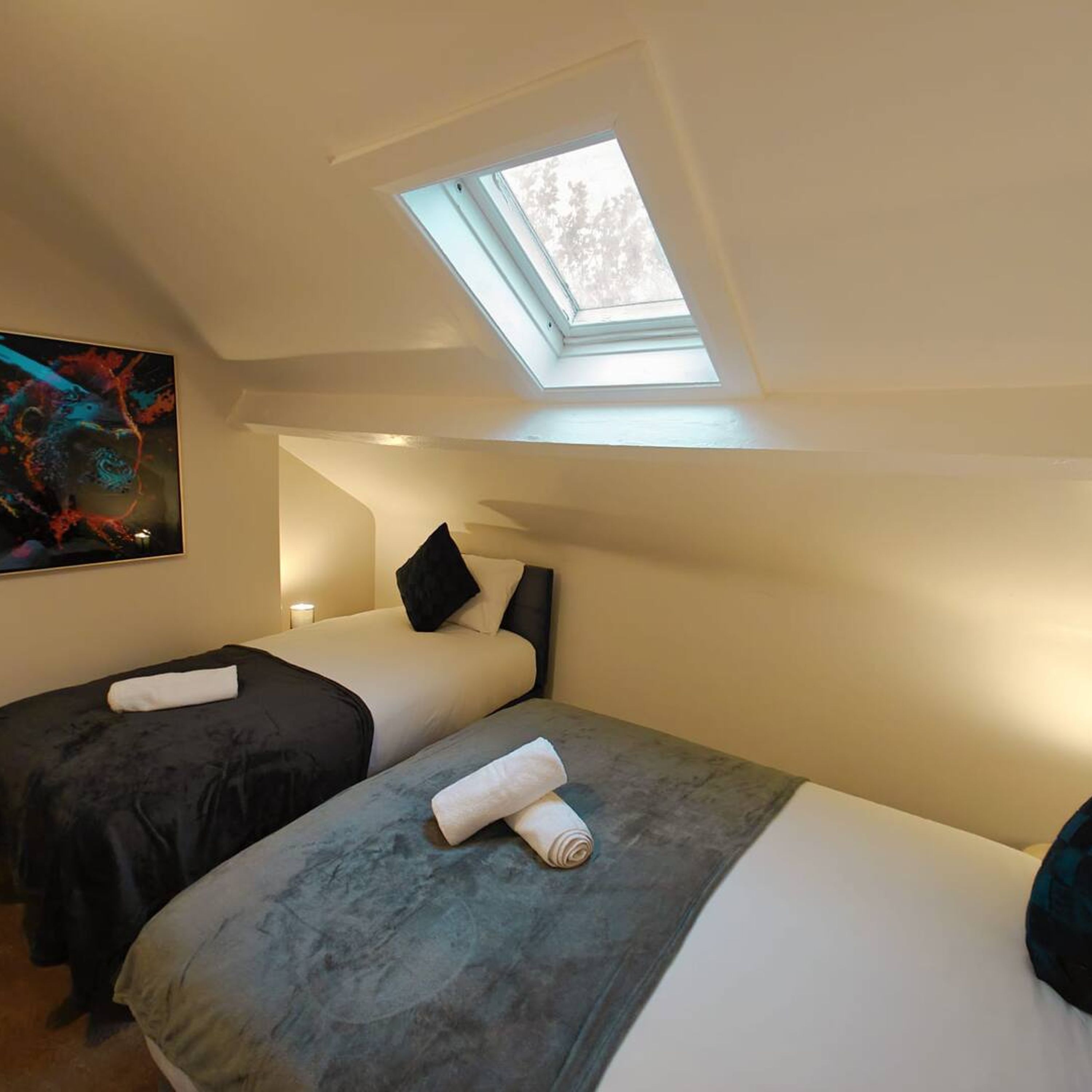 A room with two beds, a skylight, and a painting on the wall.