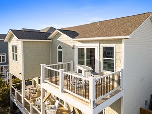 A two-story house with a balcony, a deck, and a small patio area. - Enjoy stunning ocean views at Chipps Ahoy, a spacious 4-bedroom retreat in Oak Island. (Oak Island)