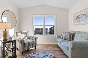 A living room with a window, a striped armchair, a sofa, a round rug, and a side table with a lamp.