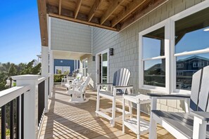 A covered outdoor deck with white railings, wooden flooring, and Adirondack chairs. - Enjoy stunning ocean views at Chipps Ahoy, a spacious 4-bedroom retreat in Oak Island. (Oak Island)