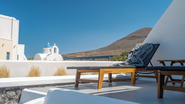 A sun lounger with a towel, a white building with blue accents, and a clear blue sky. - ACL'L Luxury Suites (Santorini)