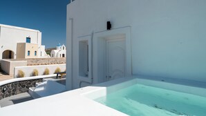 A white building with a door and a window, a stone wall, and a pool. - ACL'L Luxury Suites (Santorini)