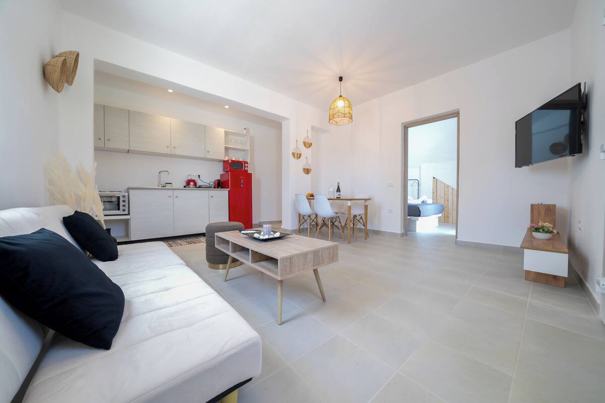 A modern living room with a white sofa, a coffee table, and a dining area with chairs and a table.