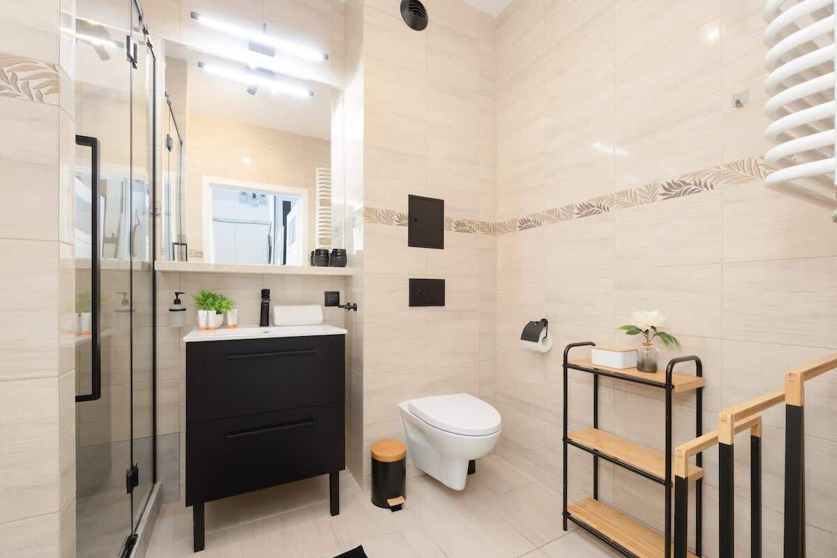 A modern bathroom with a black vanity, a white toilet, a glass shower enclosure, and a wooden shelf unit.
