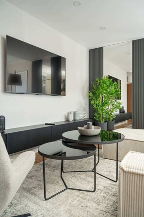 Una sala de estar moderna con un sofá, una mesa redonda con un cuenco, una planta en maceta y un espejo grande en la pared.