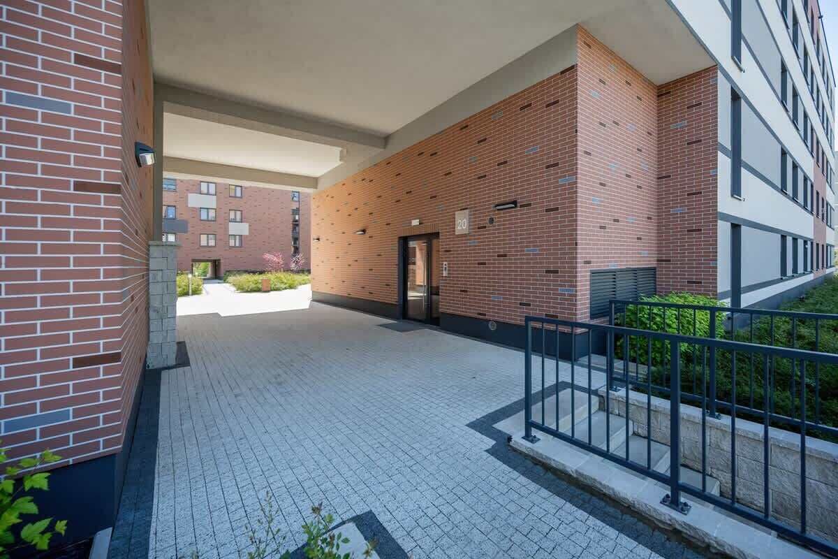 A covered outdoor area with a brick wall, a metal railing, and a paved walkway.