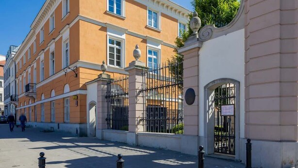 Un edificio histórico con fachada clásica, ventanas grandes y entrada protegida por una reja.
