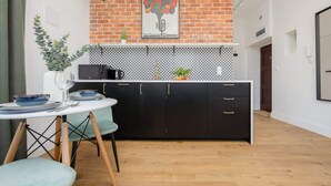 Cocina compacta con pared de ladrillo, armarios negros y encimera blanca.