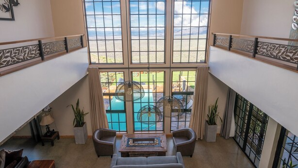 Un ampio balcone con vista sulla piscina, dotato di un'area salotto con due sedie e un tavolo, e elementi decorativi come piante in vaso e una lampada.