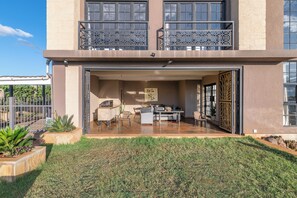 A modern two-story house with a patio area featuring outdoor furniture and a dining table.