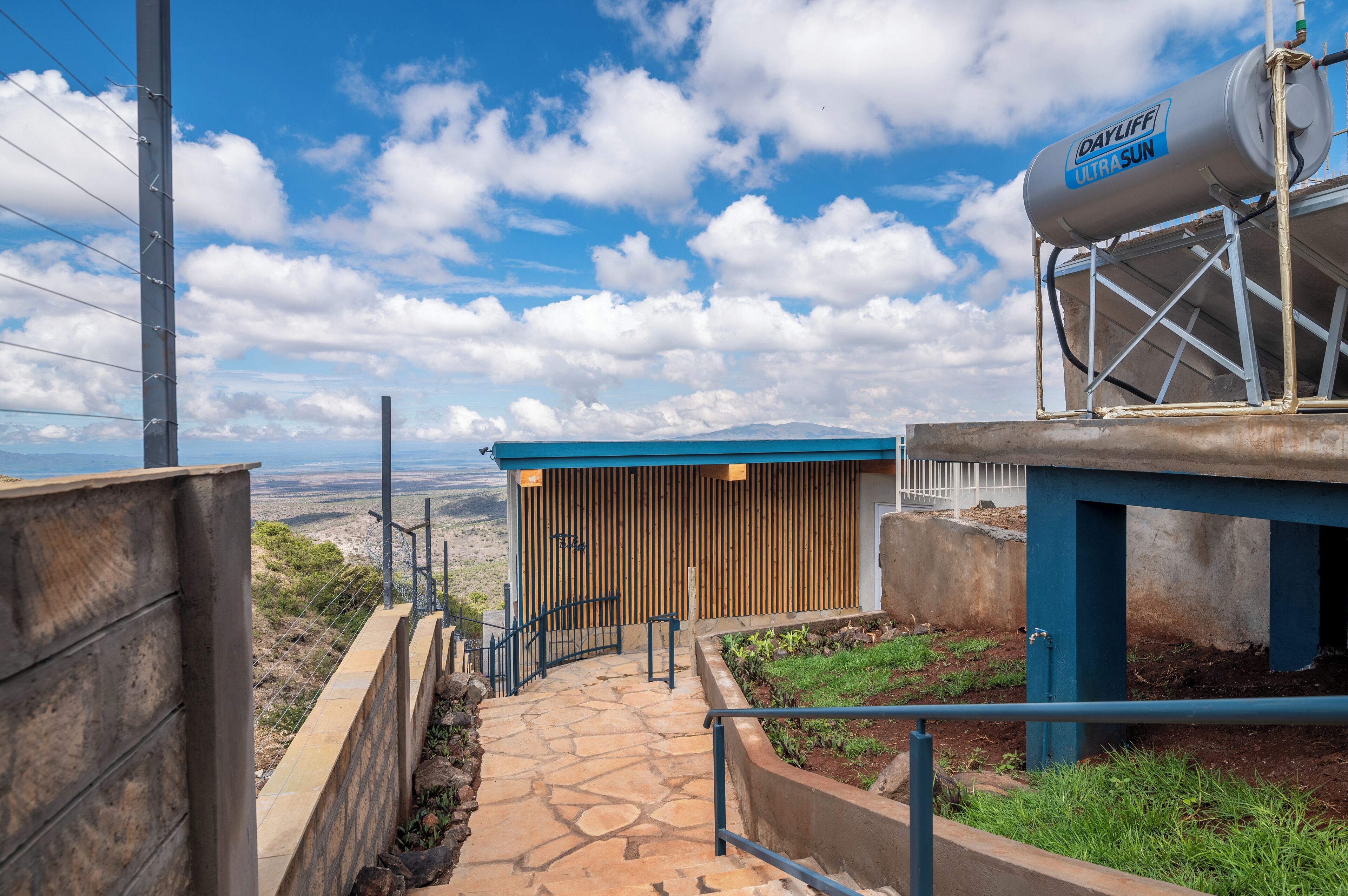 A pathway leading to a building with a blue roof and a water tank labeled "Daylife Ultrasun" on a sunny day.