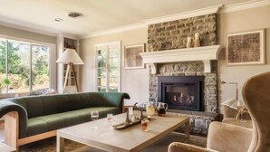 A cozy living room with a stone fireplace, a green sofa, a coffee table, and a fireplace mantel with decorative items. - The Howell House - Fire pit & spacious porch (Starkville)