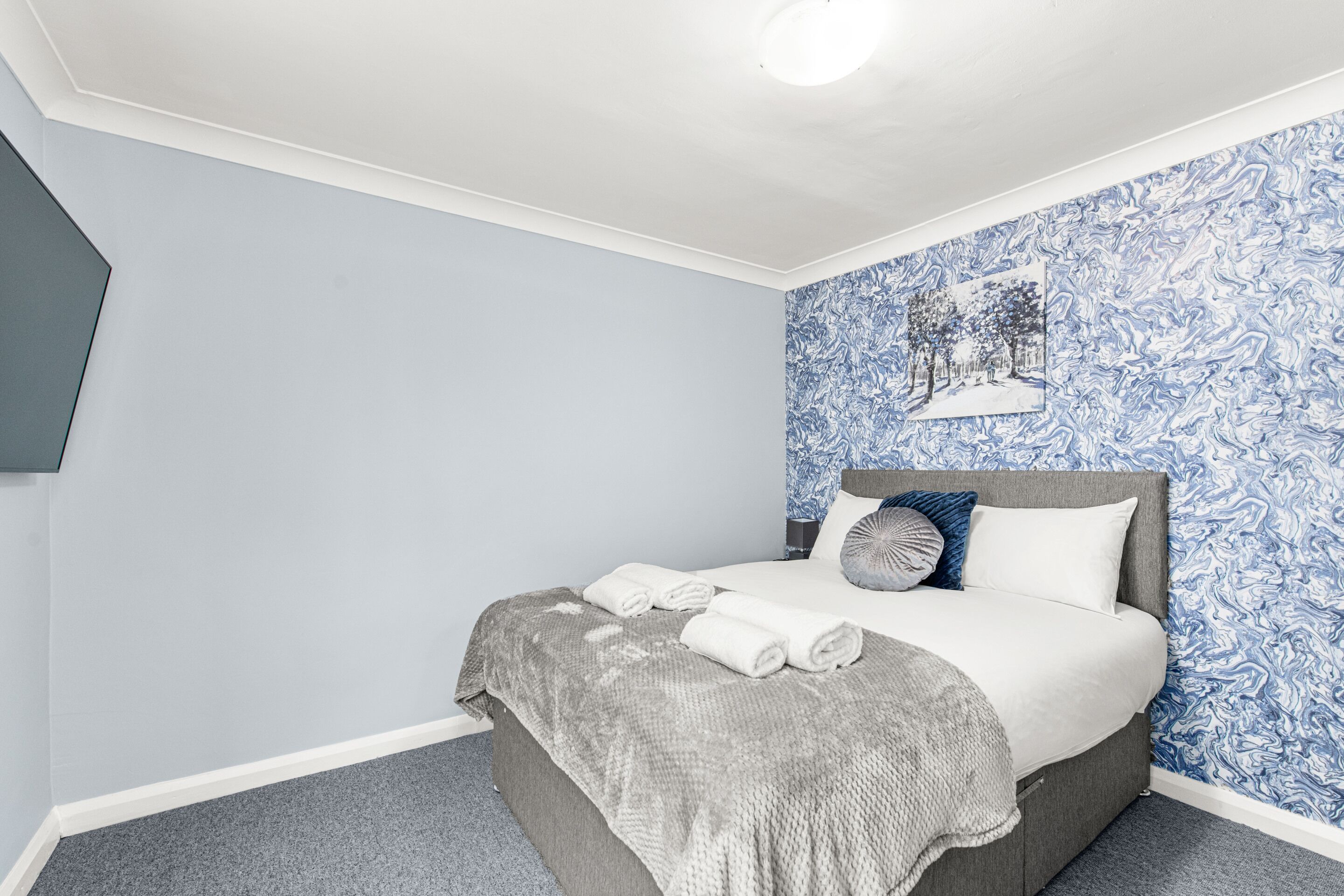 Un dormitorio con una cama, un edredón gris y una pared azul estampada.