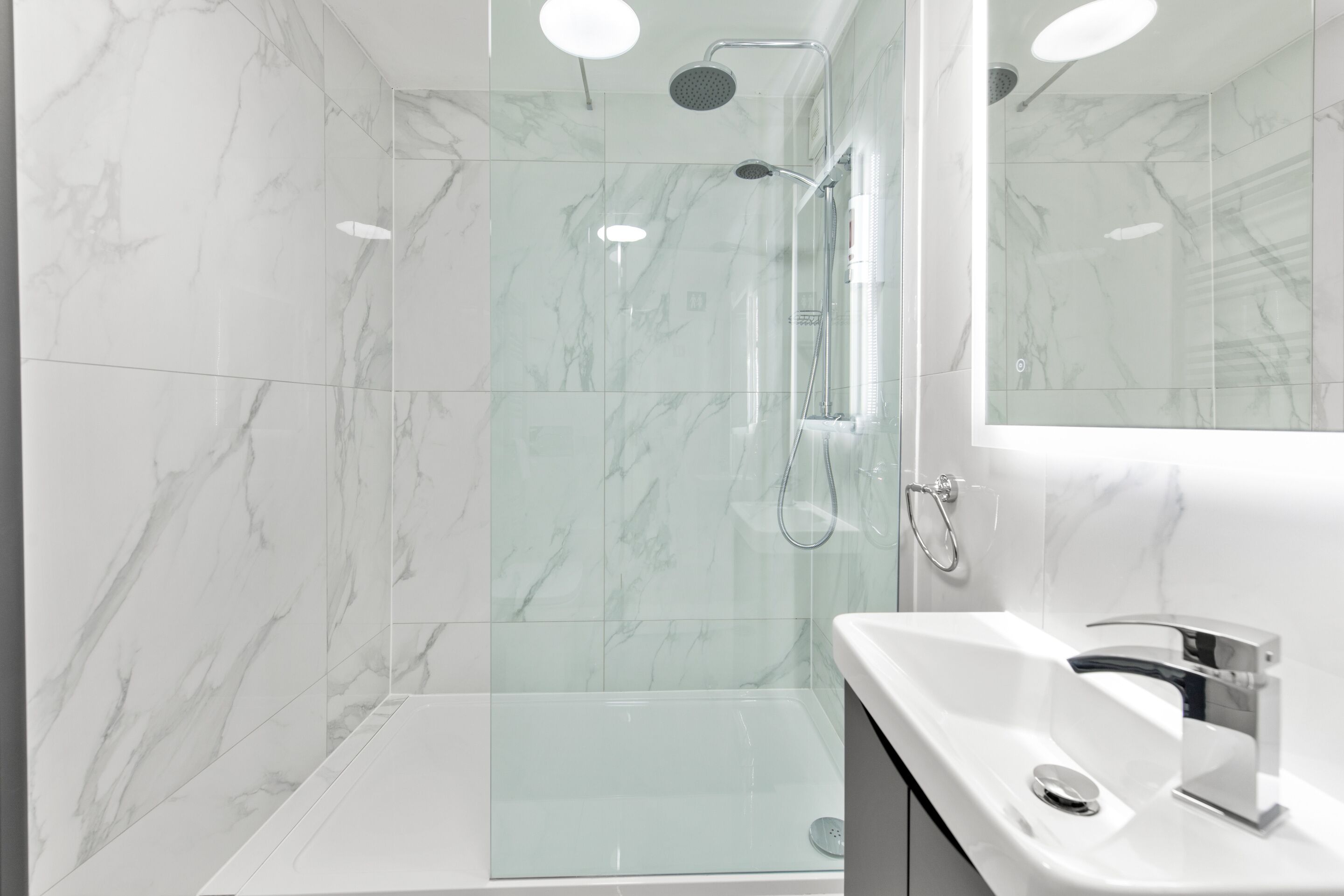 A modern bathroom with a glass-enclosed shower, a white sink, and a large mirror.