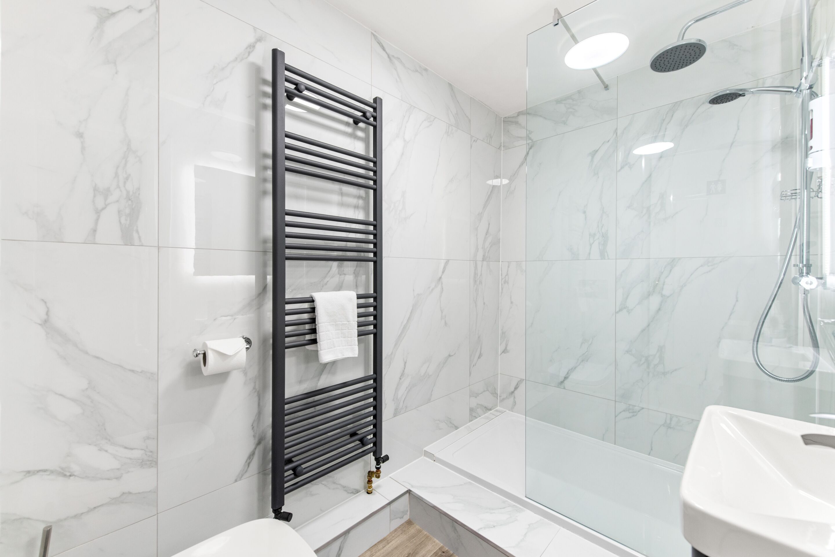 A modern bathroom with a glass shower enclosure, a black towel rack, and a white sink.