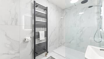 A modern bathroom with a glass shower enclosure, a black towel rack, and a white sink.