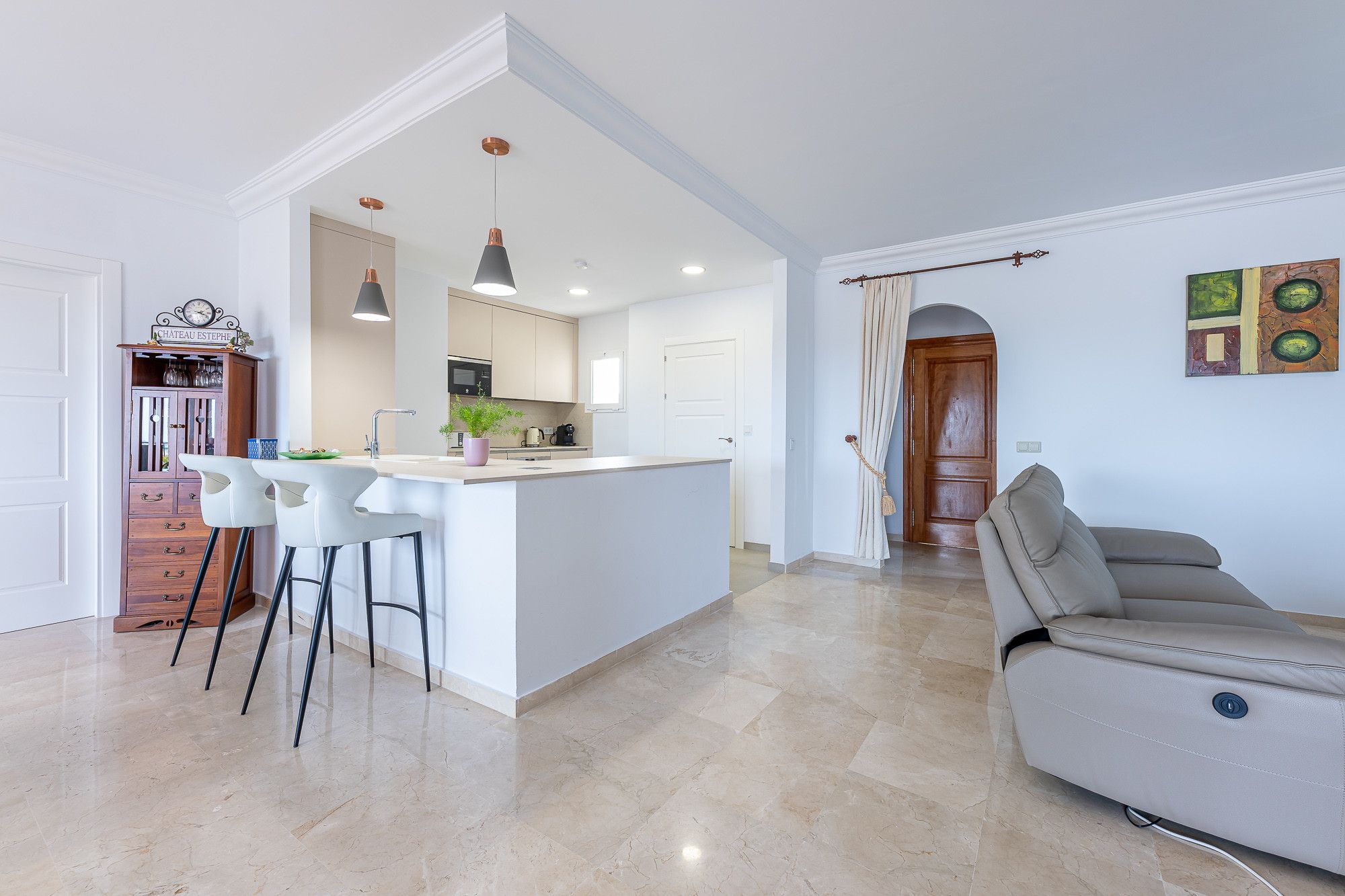 A modern kitchen with a central island, bar stools, pendant lighting, and a dining area with a sofa.