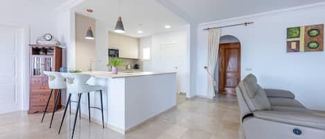 A modern kitchen with a central island, bar stools, pendant lighting, and a dining area with a sofa.