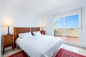 A bedroom with a wooden headboard, two bedside tables with lamps, a large bed with white bedding, and a red patterned rug.