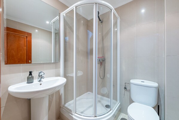 A modern bathroom with a glass-enclosed shower, a white sink, and a toilet.