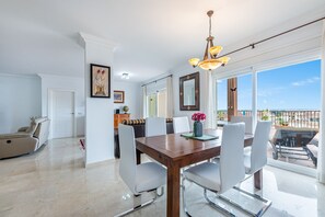 A dining area with a wooden table, white chairs, and a chandelier. There is a balcony with a view of the city.