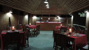 Un restaurant amb sostre i parets de fusta, taules amb mantells vermells i llums penjants.