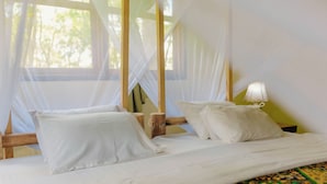 Un llit amb llençols blancs i una mosquitera, una làmpada a la paret i una catifes amb disseny.