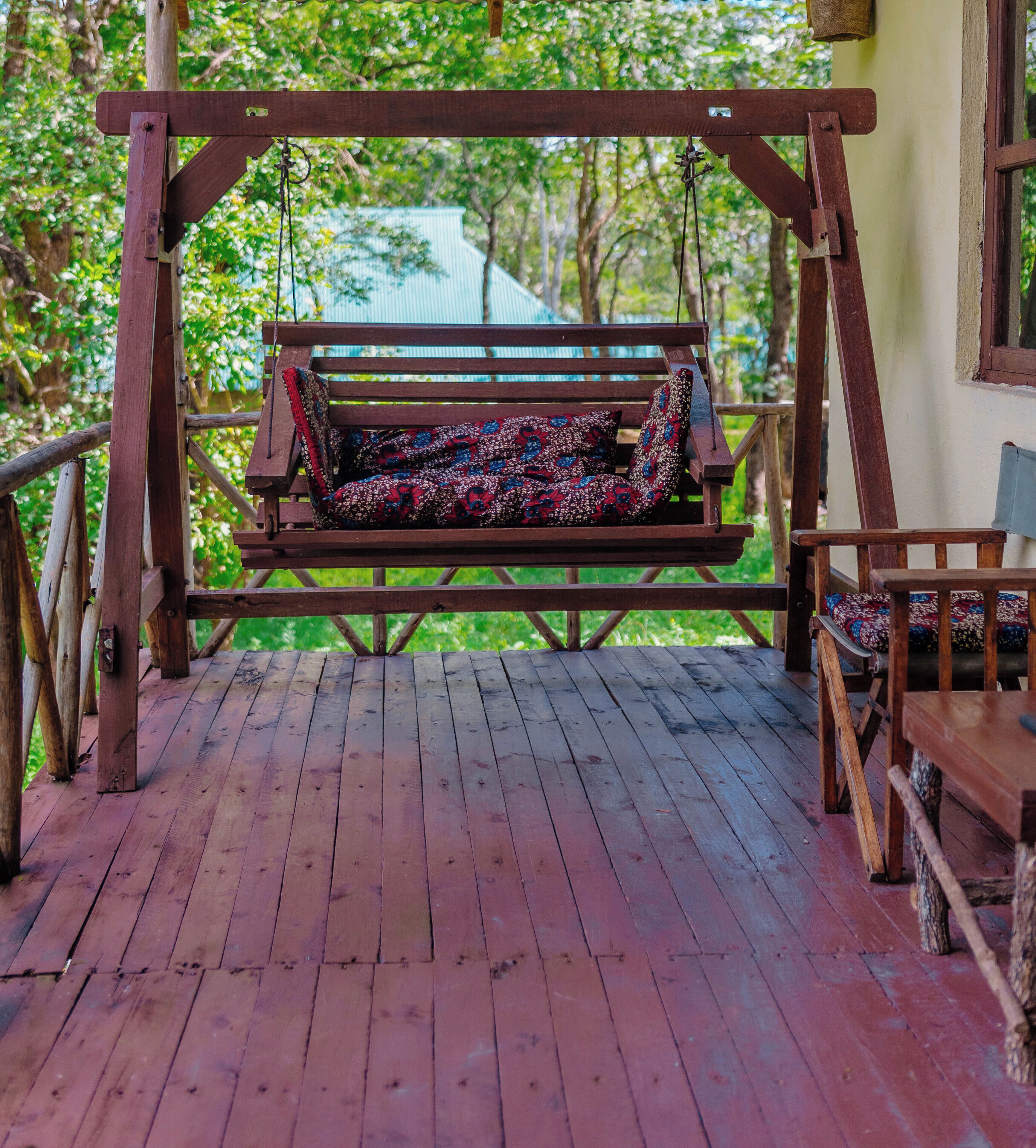 A wooden swing chair with a patterned cushion on a wooden deck.