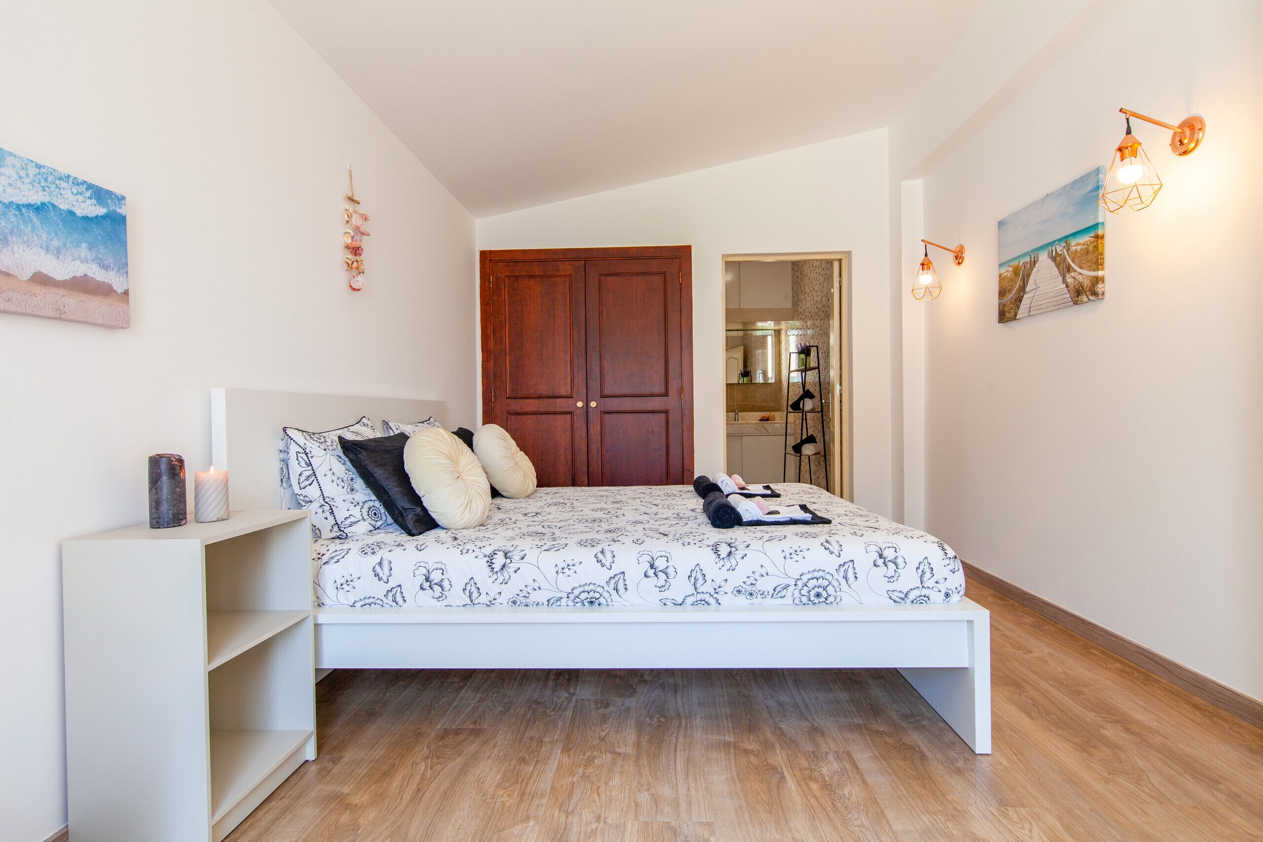 A bedroom with a bed, wooden wardrobe, and a white nightstand.