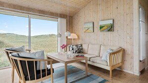 A cozy room with a wooden ceiling, a sofa, a chair, a table, and two paintings on the wall.