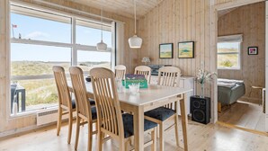 A wooden interior with a dining table, chairs, a speaker, and artwork on the walls.