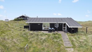 A black building with a sloped roof, a small porch with two chairs, and a car parked in the background.