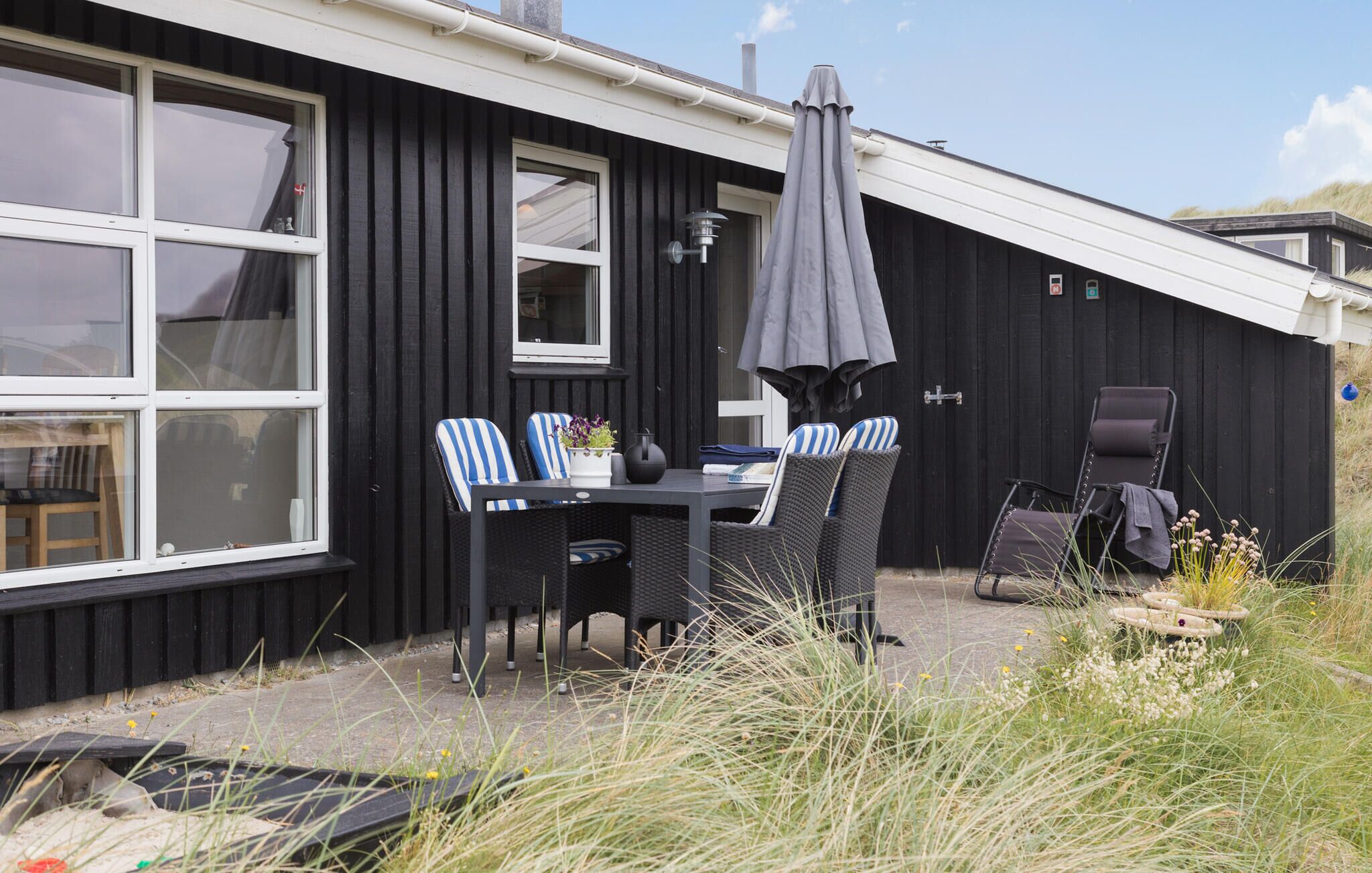 En svart byggnad med ett vitt fönsterkarm, ett bord med stolar och ett parasoll.