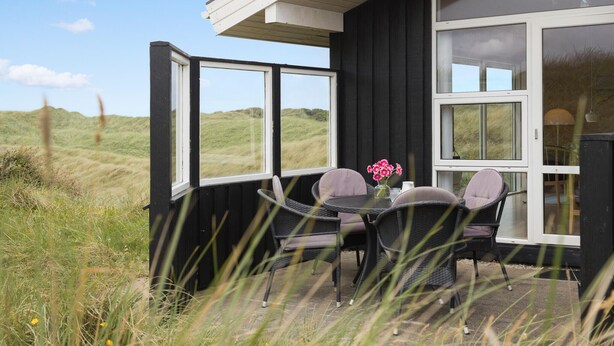 A black building with large windows and a patio area with wicker chairs and a table.