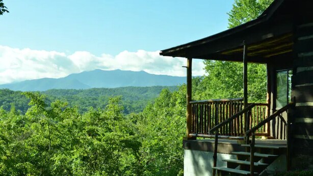 A cabin with a wooden deck and stairs leading to a porch, surrounded by lush greenery and mountains in the background. - Beautiful views from cabin in private nature reserve, 10 min to Pigeon Forge (Pigeon Forge)