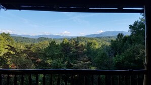 A view from a balcony with a railing, overlooking a forested landscape and distant mountains. - Beautiful views from cabin in private nature reserve, 10 min to Pigeon Forge (Pigeon Forge)