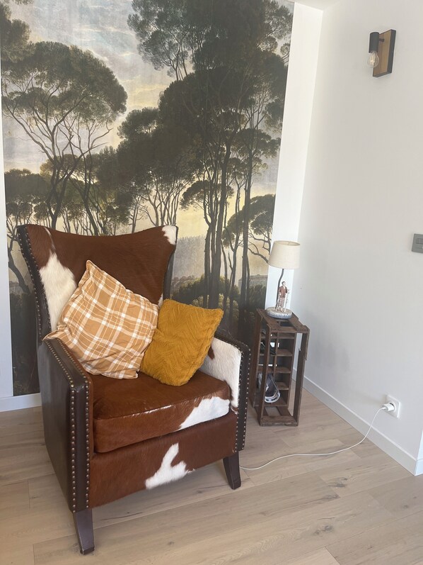 A brown leather armchair with a plaid cushion and a mustard-colored throw, positioned in front of a wall mural depicting a forest scene. - Chambres Dans Maison Neuve (Charly)