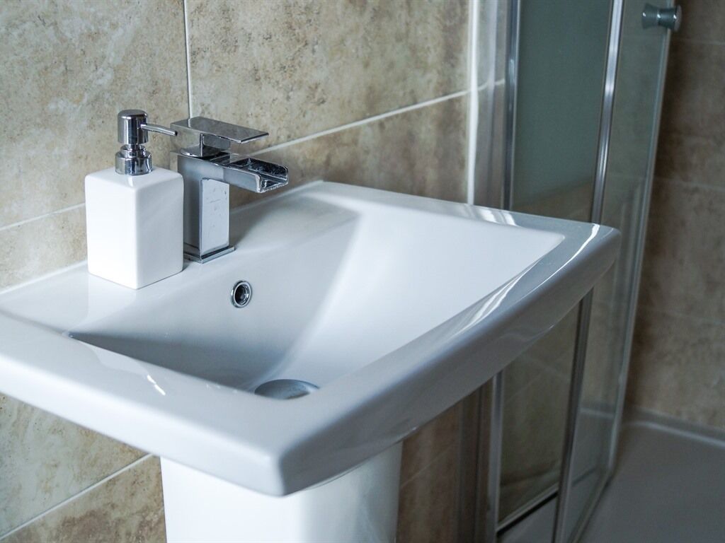 A white bathroom sink with a chrome faucet and soap dispenser.