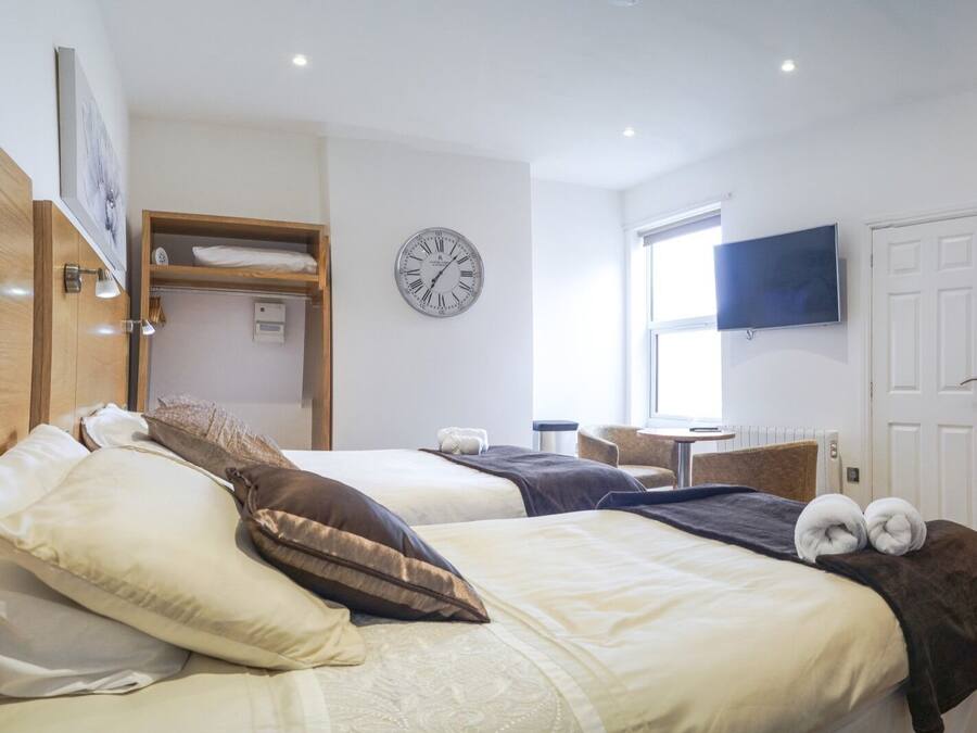 Ein Hotelzimmer mit zwei Betten, einer Wanduhr, einem Fernseher und einem Fenster.