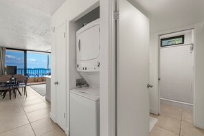 Una habitación moderna con lavadora y secadora integradas, un balcón con vistas y una puerta que da a la zona de la ducha.