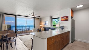 Una cocina moderna con una isla central, comedor con sillas y vistas al océano.