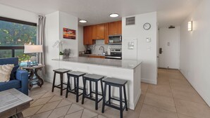 Una cocina moderna con una isla central, taburetes de bar, una zona de comedor con sofá y vistas a zonas verdes.
