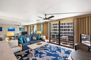 A modern hotel room with a living area, a balcony with outdoor seating, and a large window offering a city view.