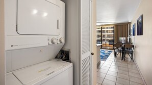 A laundry area with a front-loading washer and dryer, a door leading to a balcony with a view of buildings, and a dining area with a table and chairs.