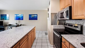 Una cocina con encimeras de granito, armarios de madera, electrodomésticos de acero inoxidable y cuadros colgados en la pared.