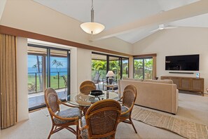 A spacious living area with a glass table, wicker chairs, a beige sofa, and a TV on a wooden cabinet. - Stunning Oceanfront 1BR/2BA Retreat with Spectacular Views - Wailea Elua 1802 (Wailea, Maui)