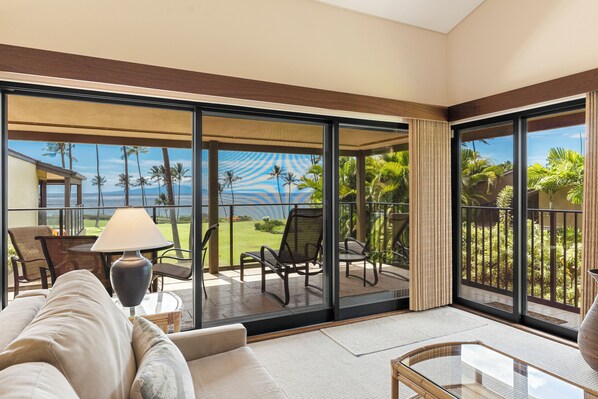 A spacious balcony with a view of palm trees and the ocean, furnished with a sofa, chairs, and a table.