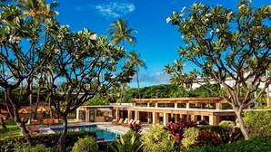 Een resort met een zwembad, palmbomen en een modern gebouw met een overdekt buitengebied.