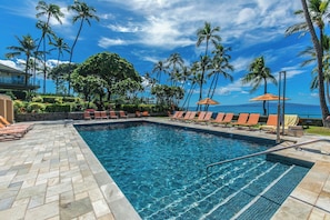 A swimming pool with lounge chairs and umbrellas, surrounded by palm trees and a view of the ocean. - Stunning Oceanfront 1BR/2BA Retreat with Spectacular Views - Wailea Elua 1802 (Wailea, Maui)