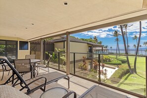 Un balcon avec vue sur l’océan et les palmiers, aménagé avec des chaises et une table.